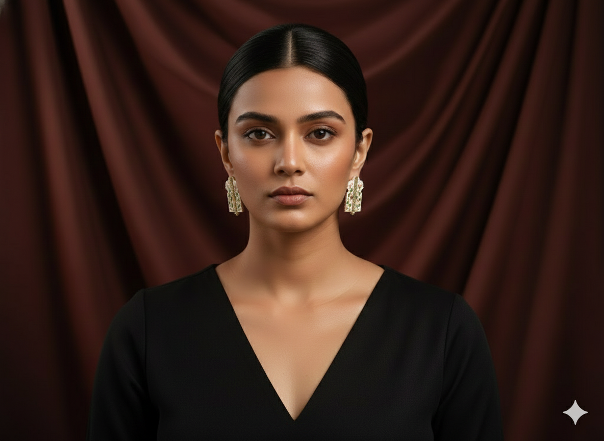 Woman wearing a black top and gold earrings against a brown curtain background